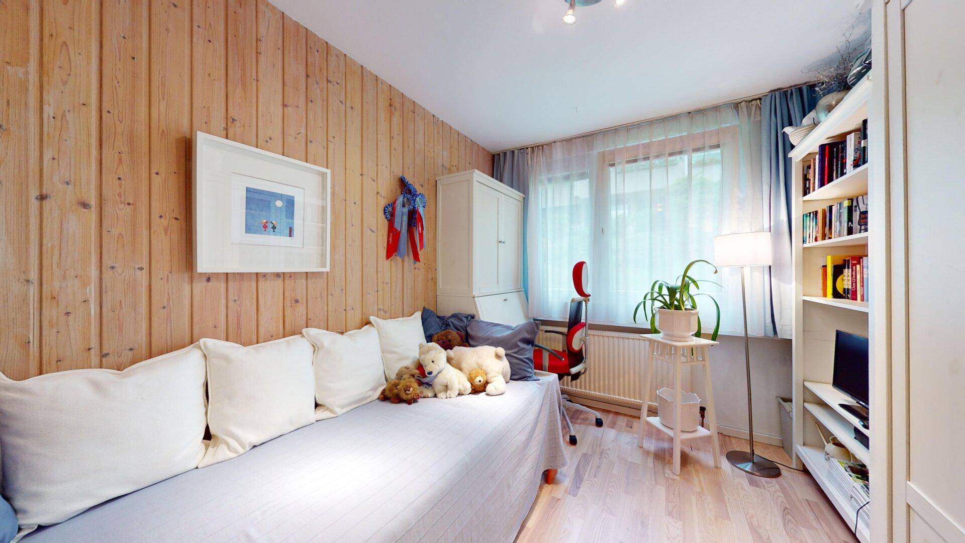 Schlafzimmer mit Holzwänden, Einzelbett und Blick ins Grüne, gemütlich und hell.