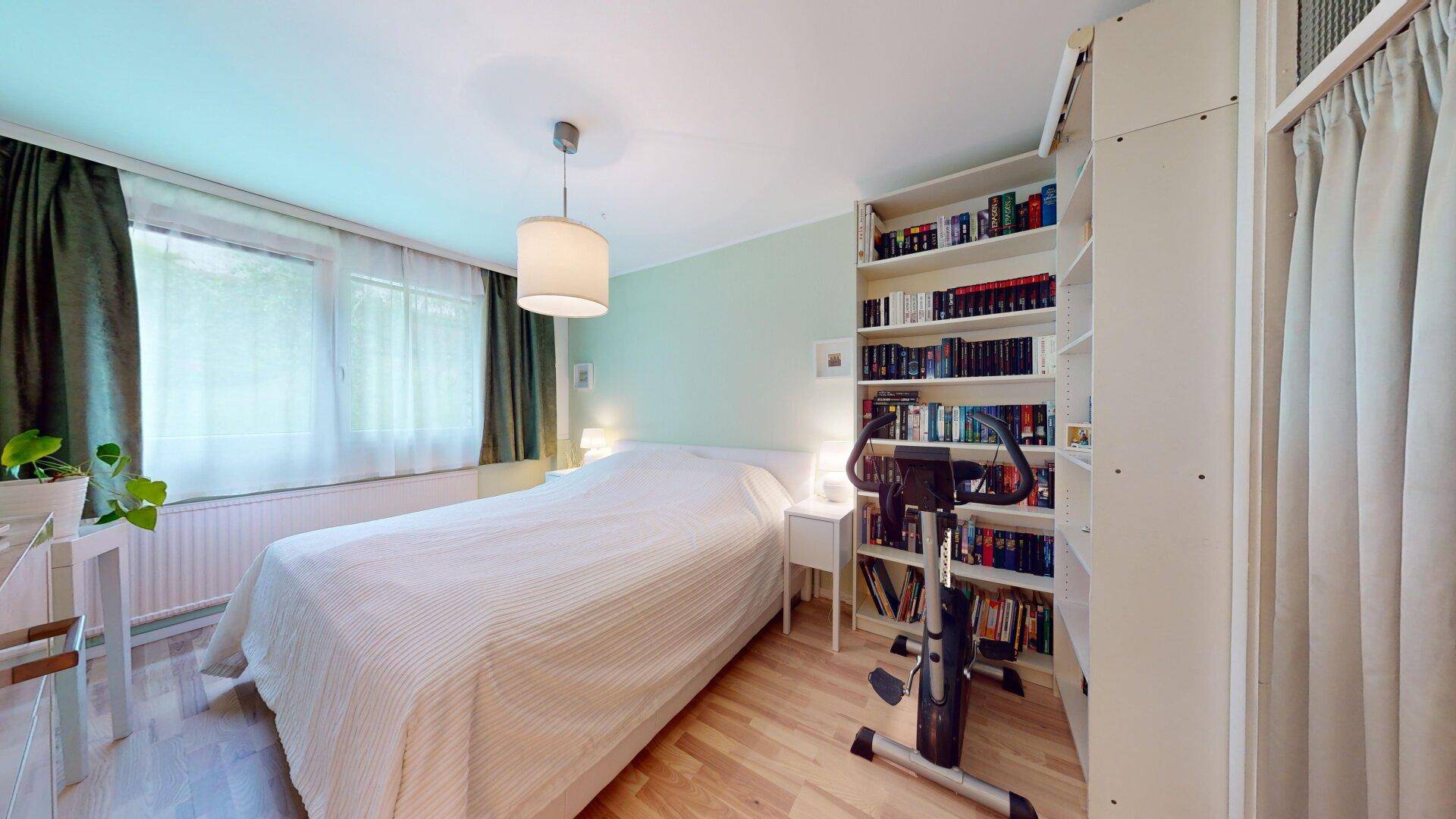 Helles Schlafzimmer mit Doppelbett, Bücherregal und Trainingsgerät, bietet Platz für Hobbys.