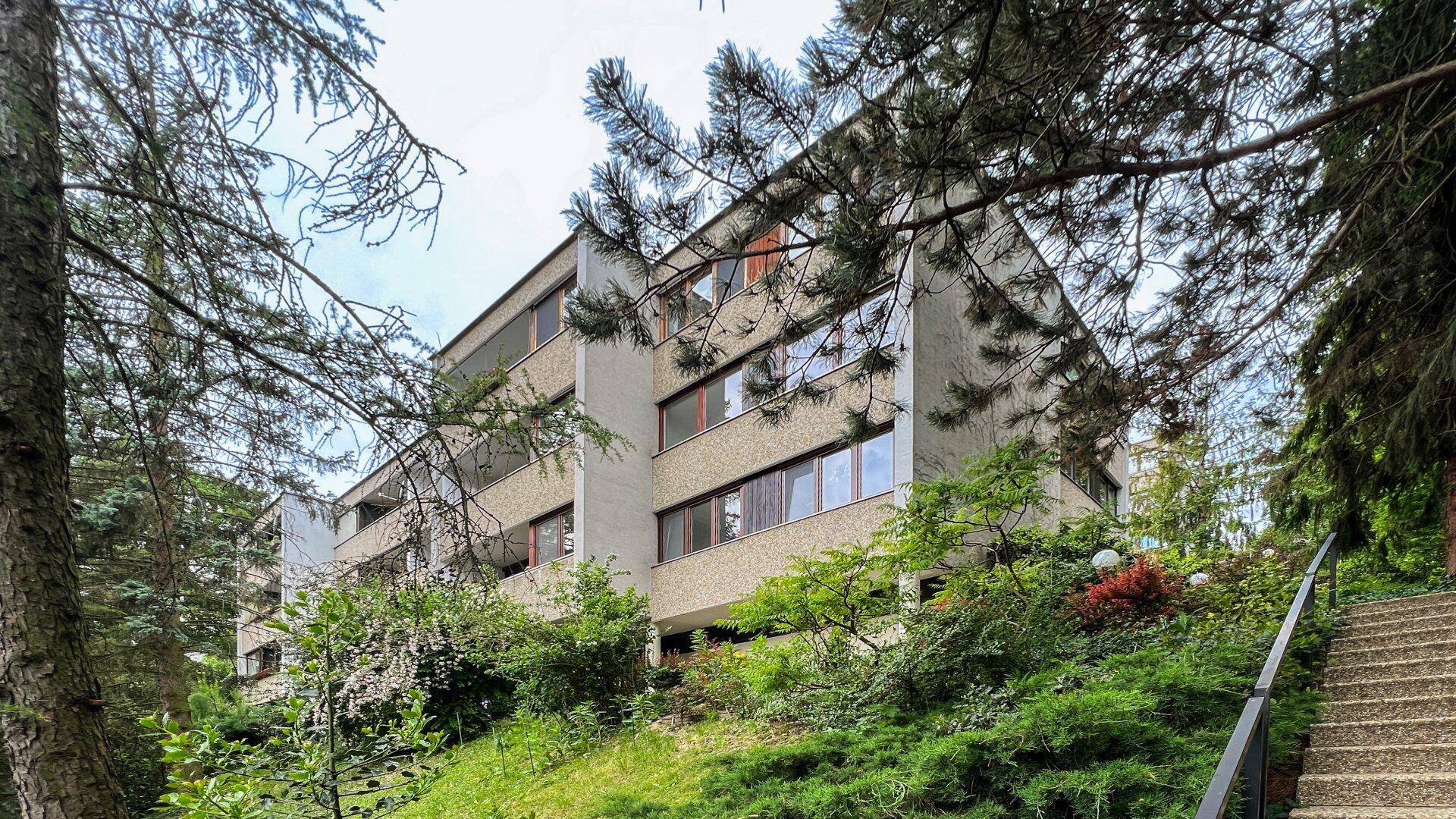 Moderne Architektur des Gebäudes, eingebettet in eine grüne Hügellandschaft, mit vielen Bäumen.