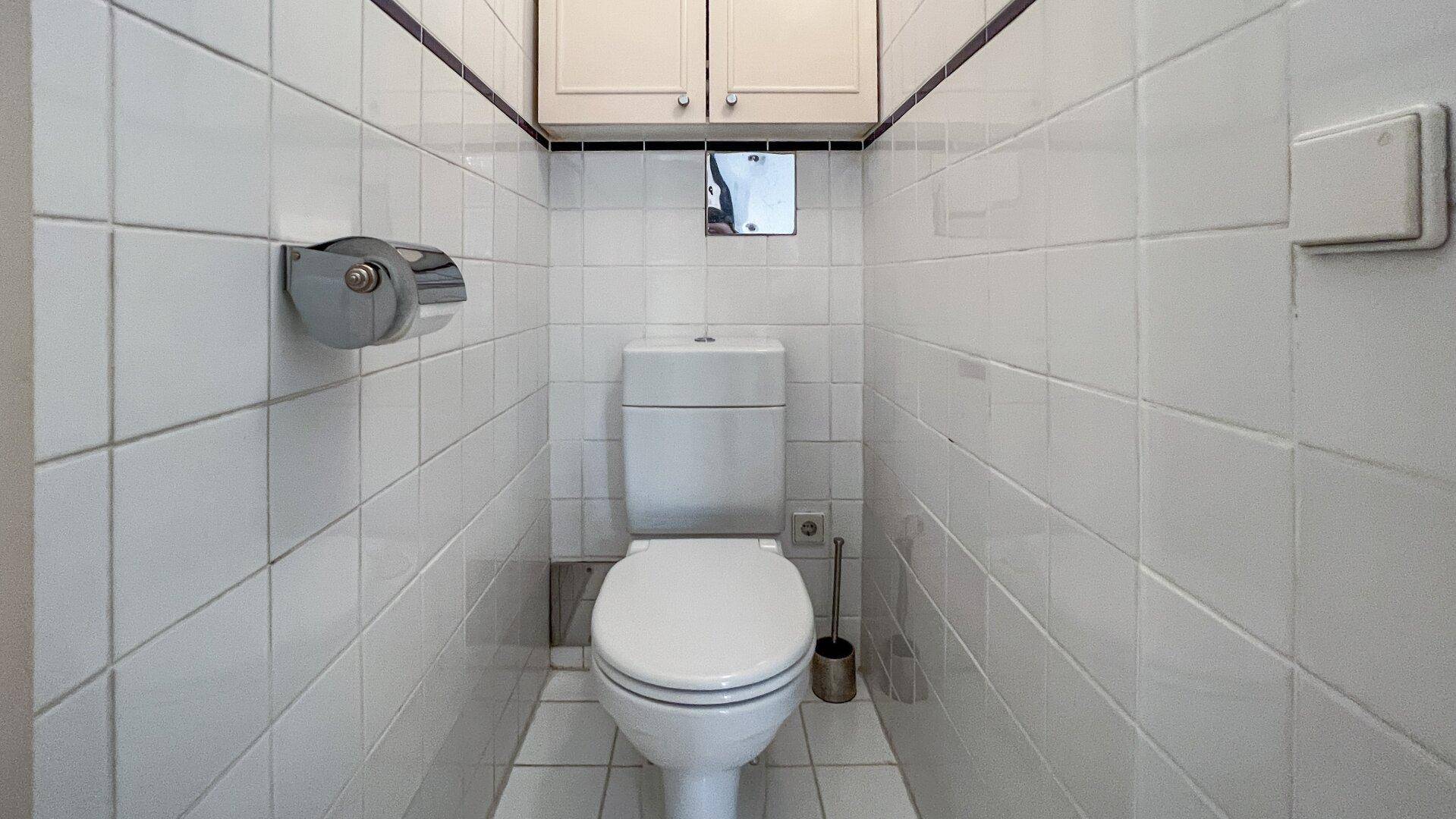 Kleines Gäste-WC mit weißen Fliesen und wandmontierter Toilette, sauber und funktional.