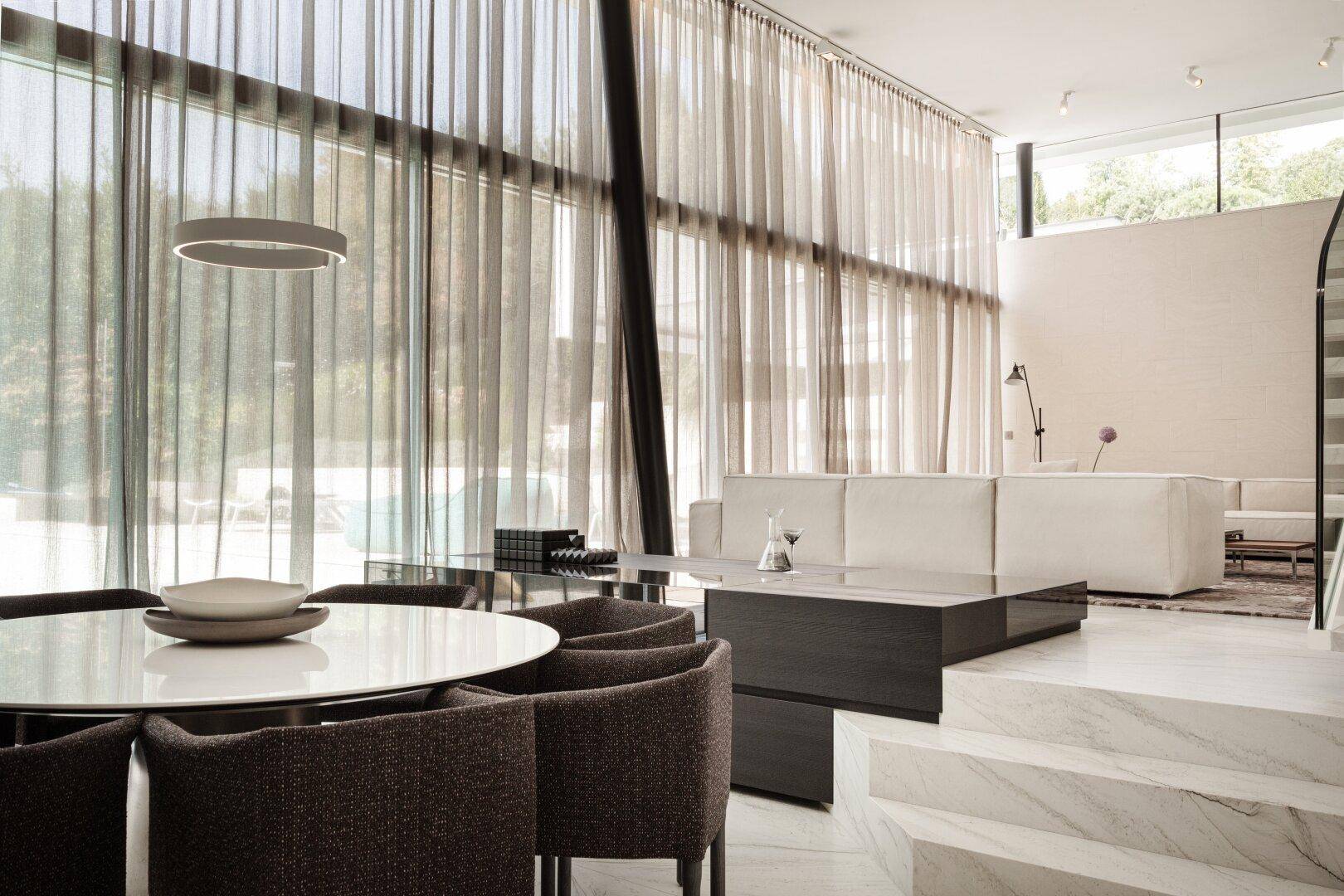 Lichtdurchfluteter Wohn- und Essbereich mit bodentiefen Fenstern, eleganten Vorhängen und modernem Design.