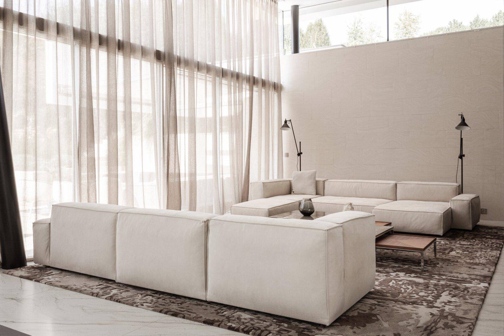 Geräumiges Wohnzimmer mit bequemen Sofas, großem Teppich und viel natürlichem Licht durch die Fenster.