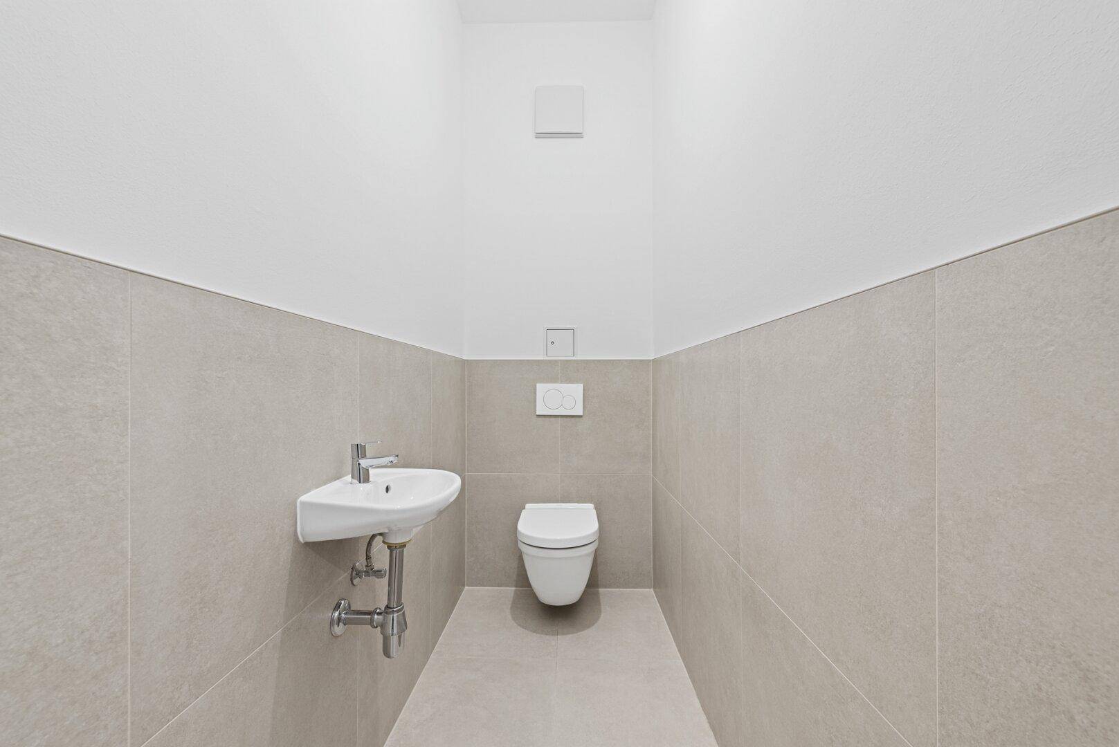 Modern geflieste Gästetoilette mit wandhängendem WC und kleinem Waschbecken.