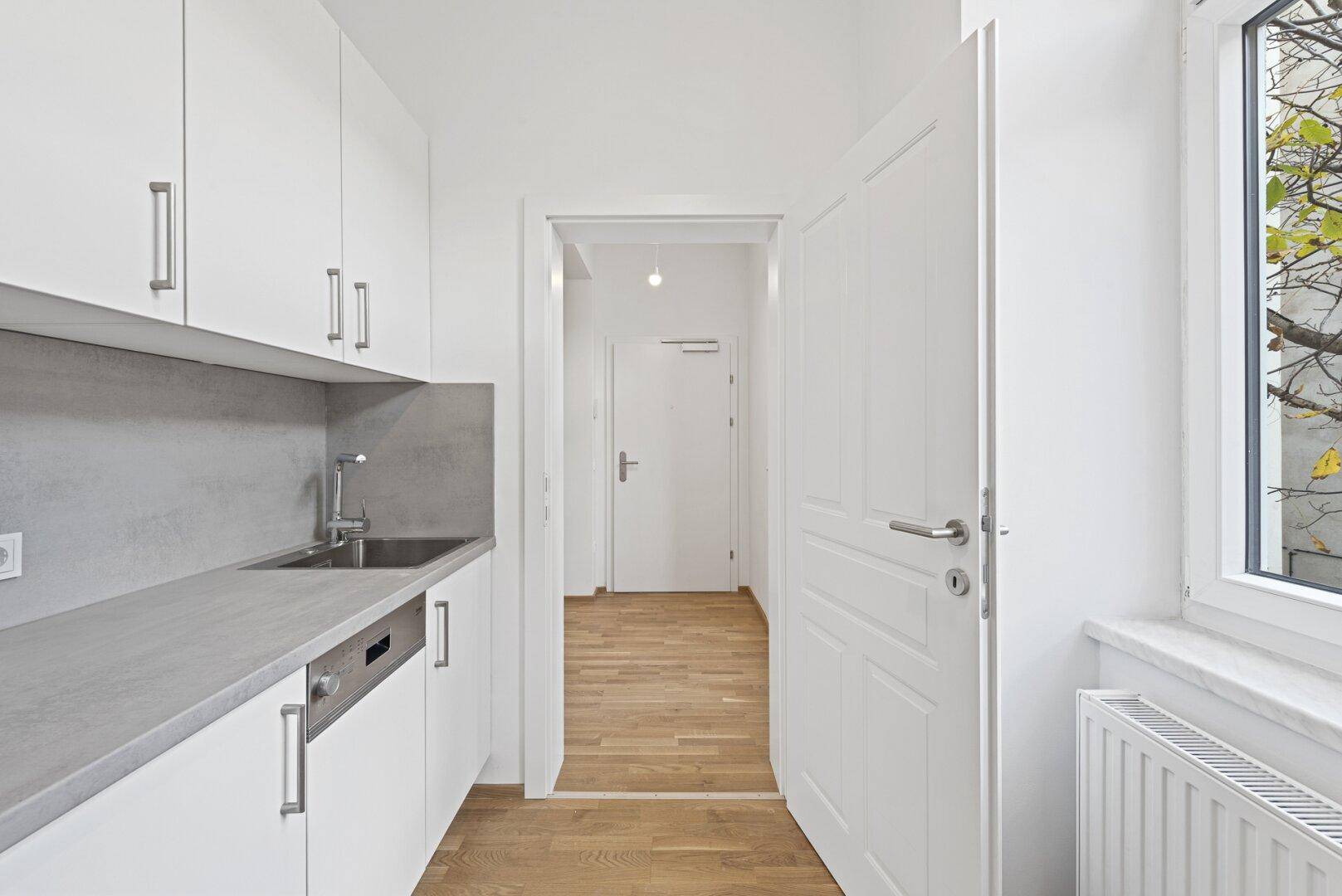 Moderne Küche mit weißen Schränken, Spülmaschine und Fenster mit Blick nach draußen.
