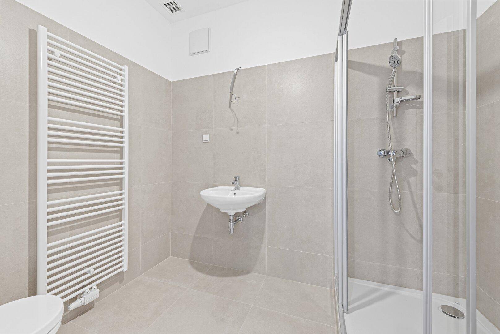 Helles Badezimmer mit Duschkabine, Waschbecken und großem beheiztem Handtuchhalter.
