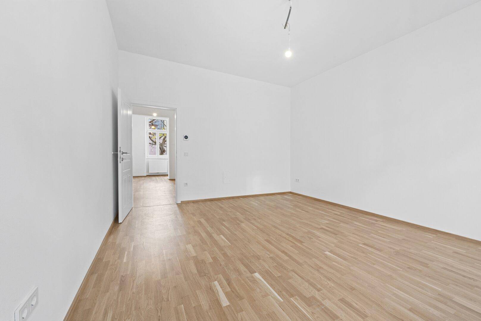 Heller Raum mit Parkettboden und Zugang zu einem weiteren Zimmer.