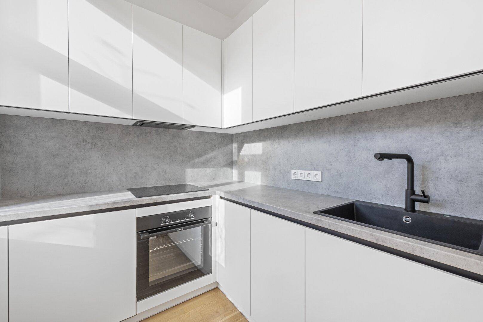 Moderne Einbauküche mit weißen Schränken, grauer Arbeitsplatte und schwarzer Spüle.