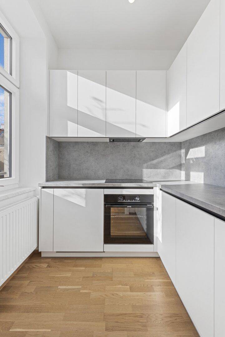Moderne Küche mit weißen Schränken, Holzboden und Fenster für natürliches Licht.