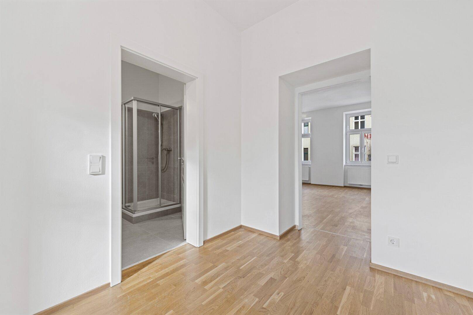 Heller Raum mit Parkettboden und Zugang zu einem Badezimmer und einem weiteren Zimmer.