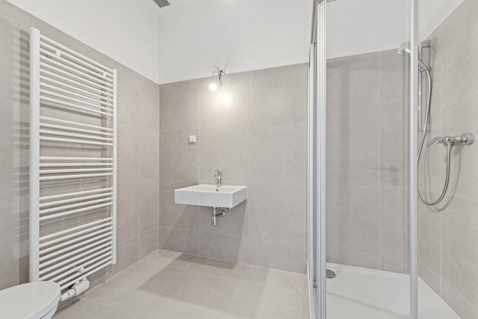 Modernes Badezimmer mit grauen Fliesen, Duschkabine und beheiztem Handtuchhalter.