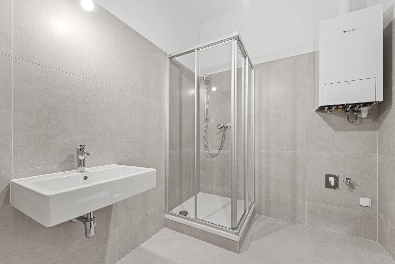 Funktionales Badezimmer mit Duschkabine, Waschbecken und an der Wand montiertem Warmwasserbereiter.