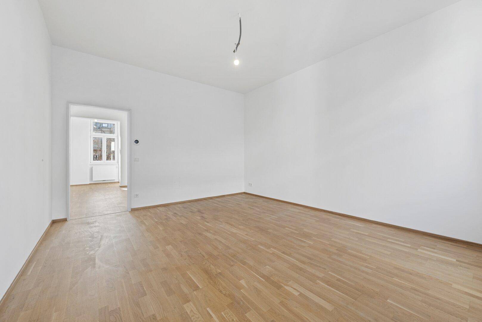 Leerer, heller Raum mit Parkettboden und offenem Zugang zu einem weiteren Zimmer.