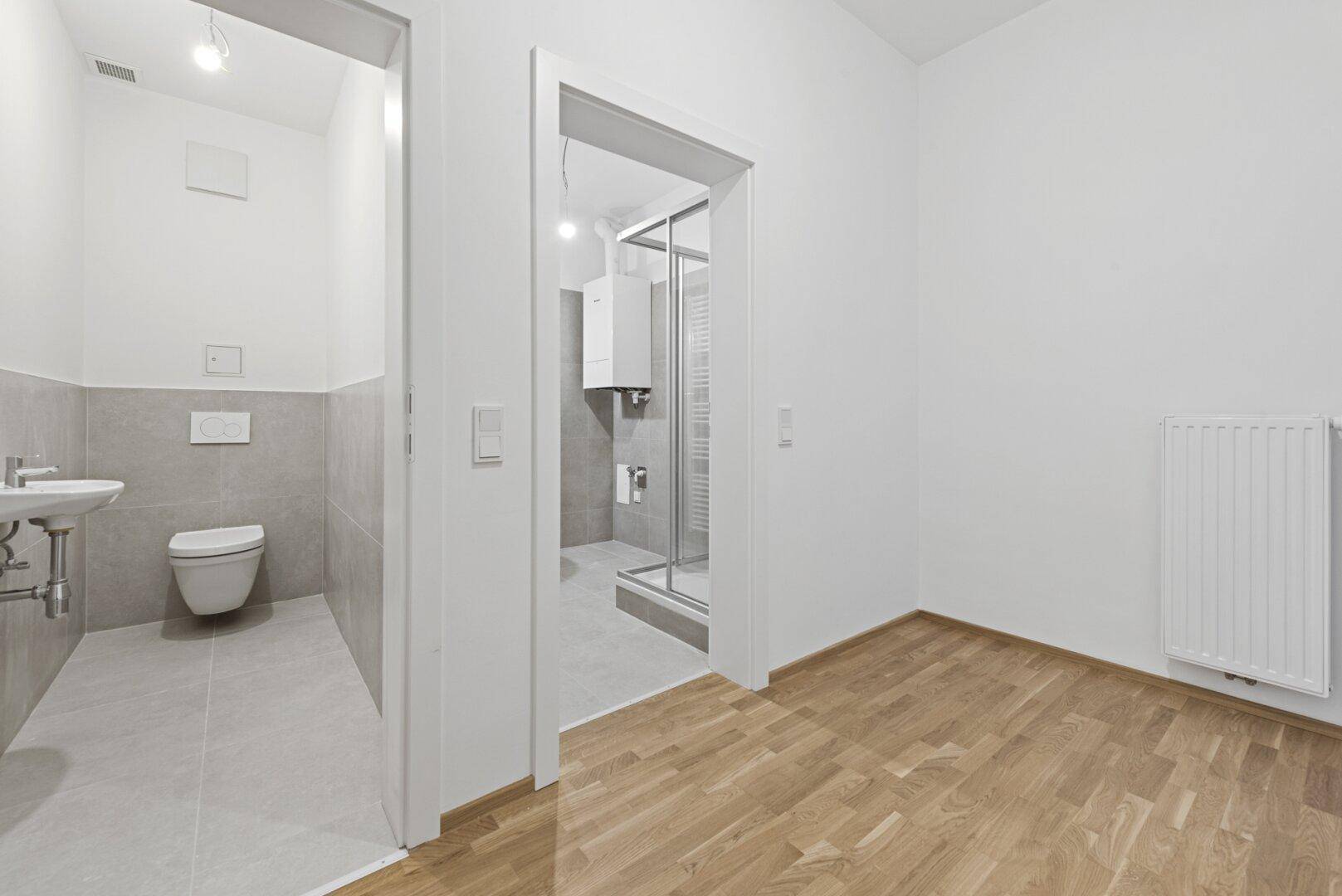 Heller Raum mit Holzboden und Zugang zu einem Gäste-WC und einem Duschbad.