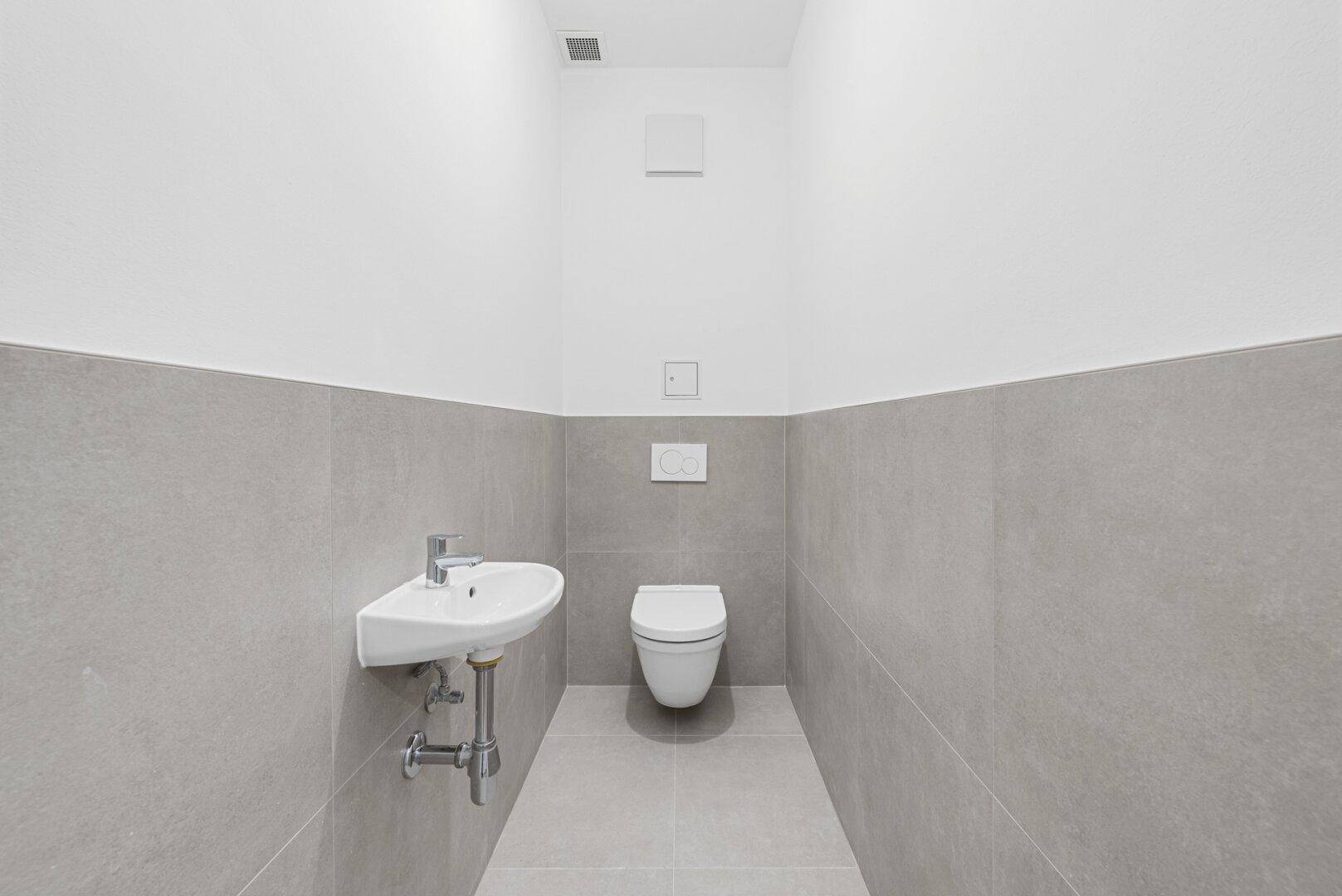Modernes Gäste-WC mit grauen Fliesen, wandhängender Toilette und kleinem Waschbecken.