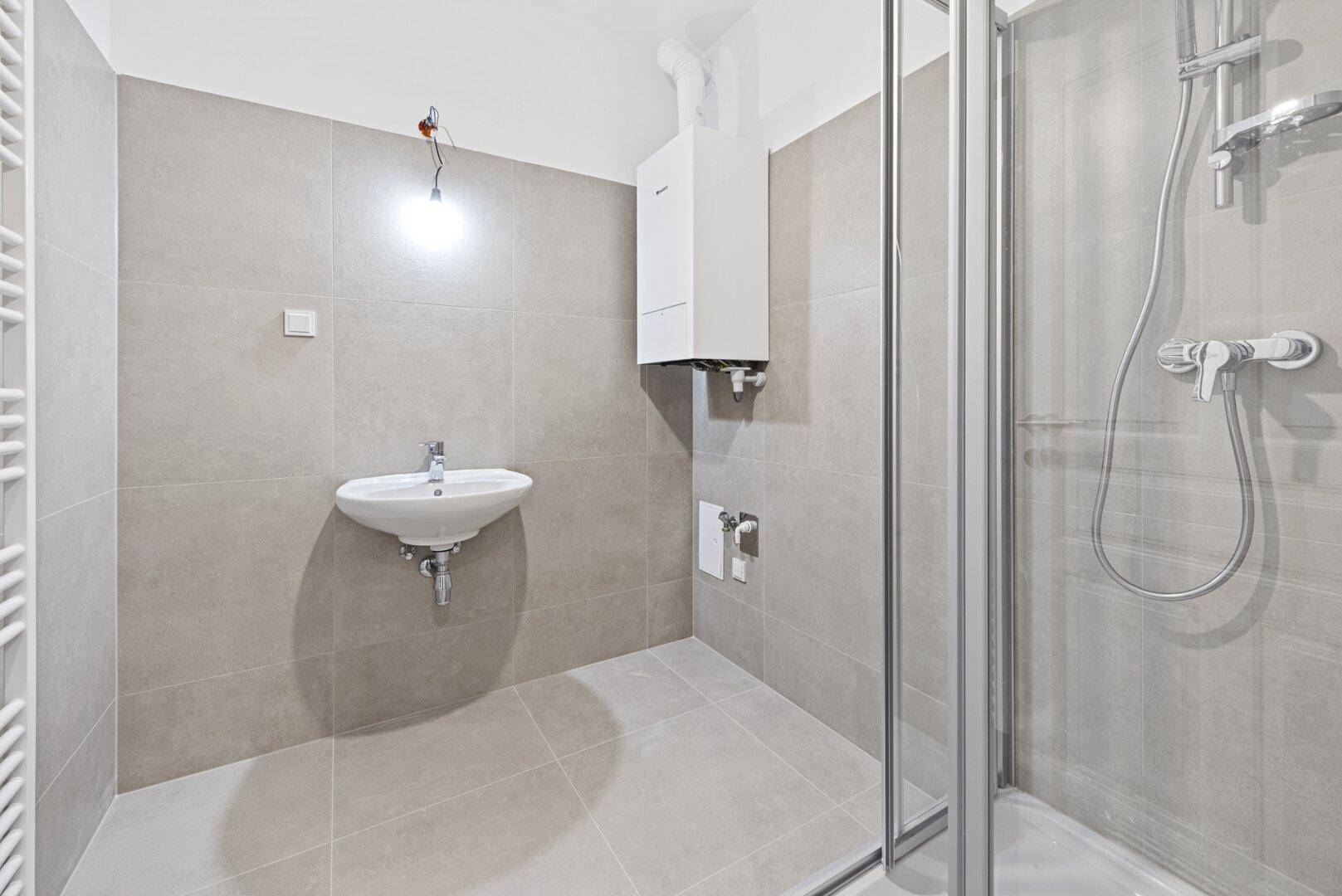 Funktionales Badezimmer mit Duschkabine, Waschbecken und Warmwasserbereiter, komplett gefliest.