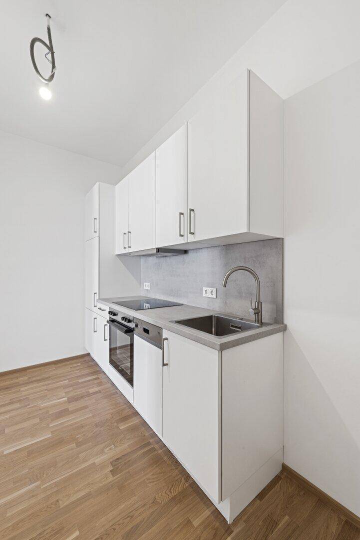 Kompakte Einbauküche mit weißen Fronten, integriertem Backofen und Induktionskochfeld.