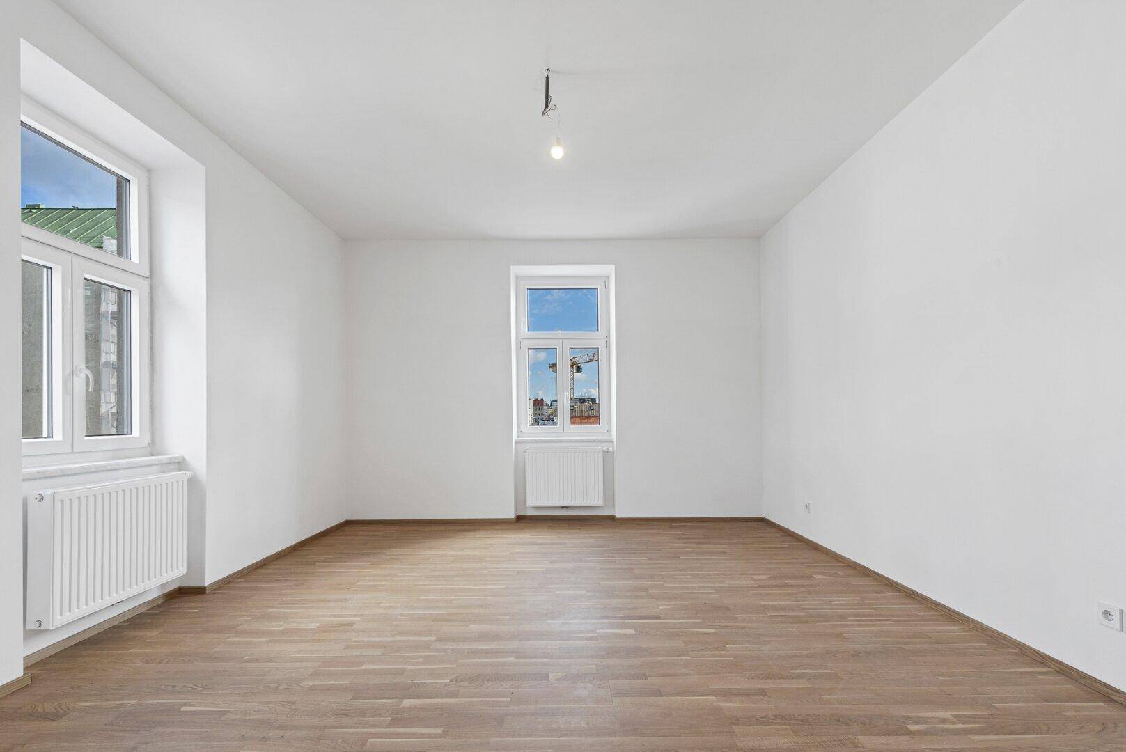 Helles Schlafzimmer mit Holzboden und zwei Fenstern, die viel Tageslicht hereinlassen.