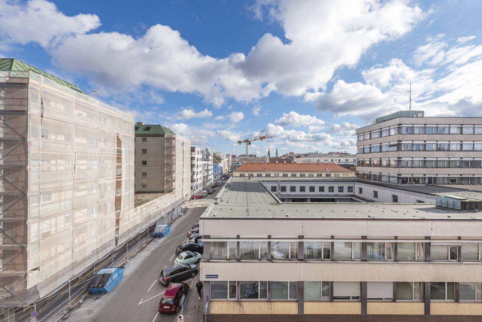 Weitläufiger Blick über eine Stadtstraße mit Gebäuden, Fahrzeugen und einer Baustelle.