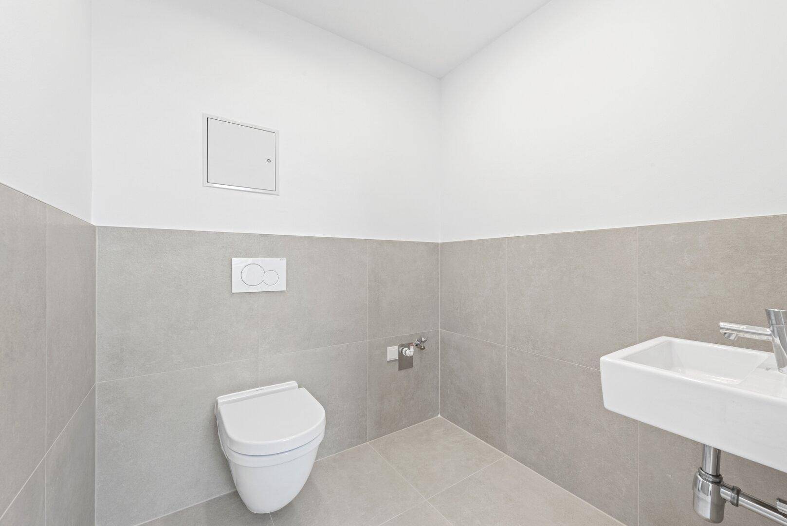 Modernes Gäste-WC mit hellgrauen Fliesen, wandhängendem WC und kleinem Waschbecken.