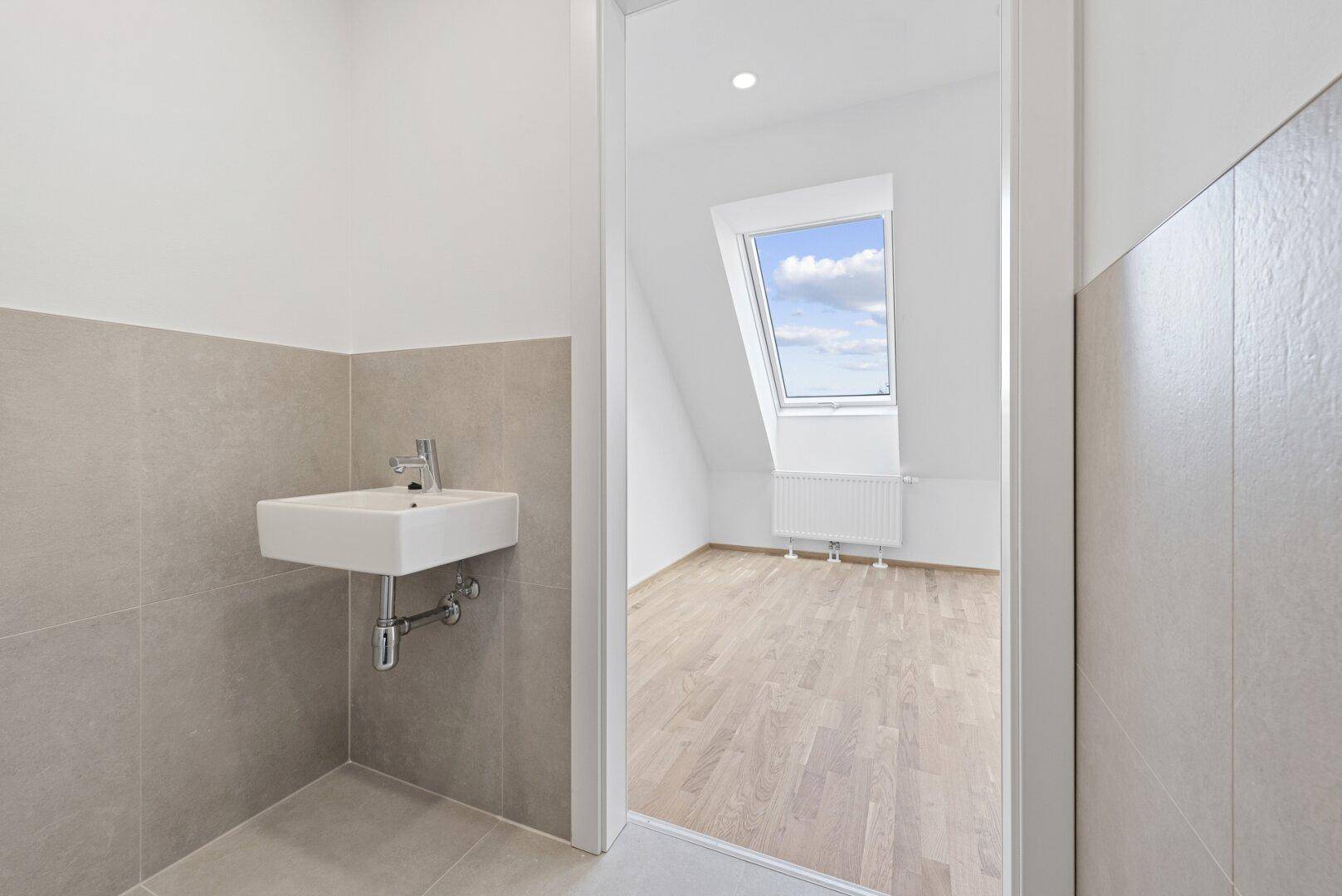Eingangsbereich zum Gäste-WC mit Waschbecken und Blick in einen hellen Raum mit Dachfenster.