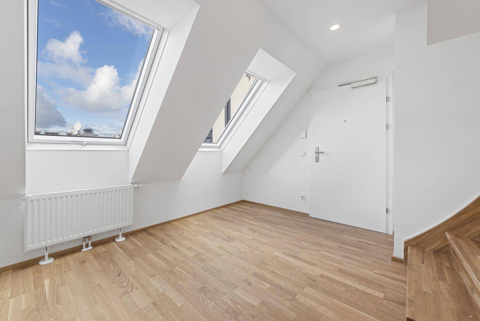 Heller Eingangsbereich mit Holzboden, Dachfenstern und weißer Eingangstür im Dachgeschoss.