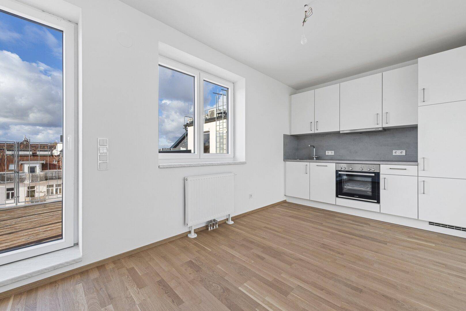 Helle Küchenzeile in offenem Raum mit Zugang zu einem Balkon und Holzboden.