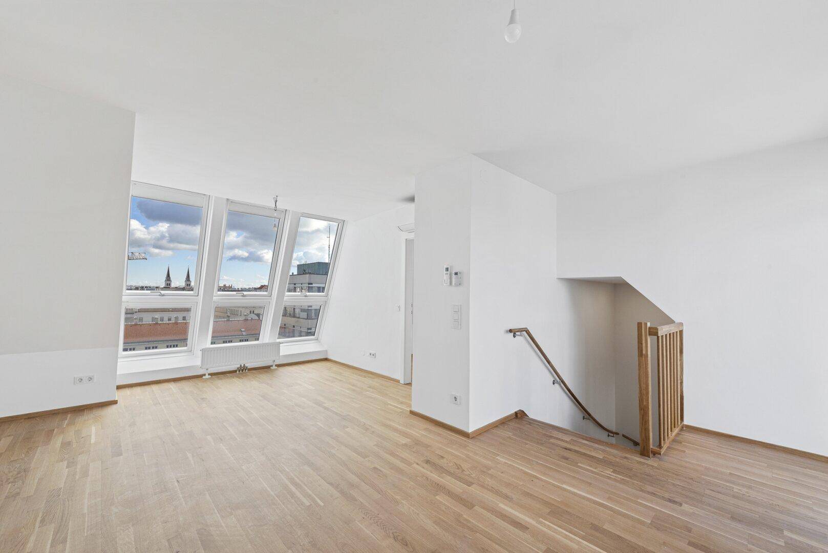 Geräumiger Wohnbereich mit Holzboden, großen Dachfenstern und Panoramablick über die Stadt.