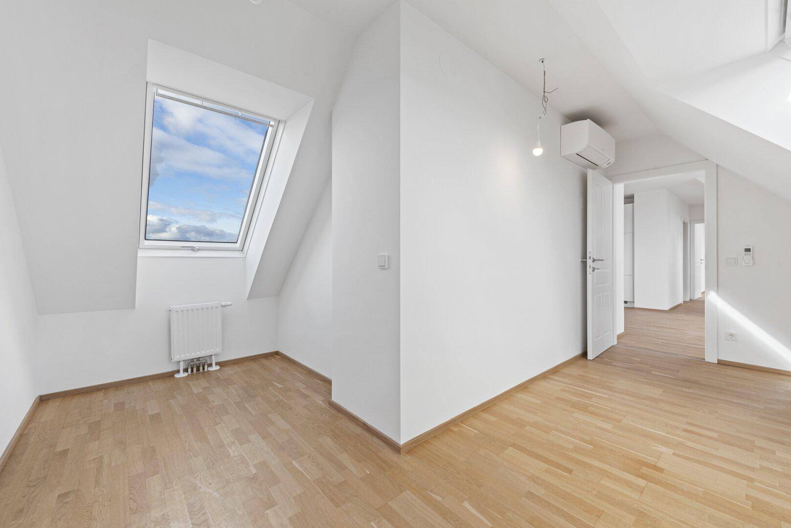 Heller Raum mit Holzboden, Dachfenster, Klimaanlage und Zugang zu anderen Bereichen.