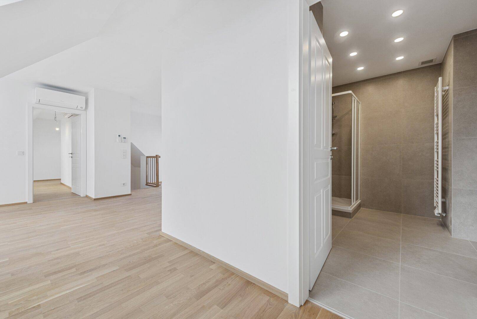 Heller Flurbereich mit Holzboden und offenem Zugang zu einem modernen Badezimmer.