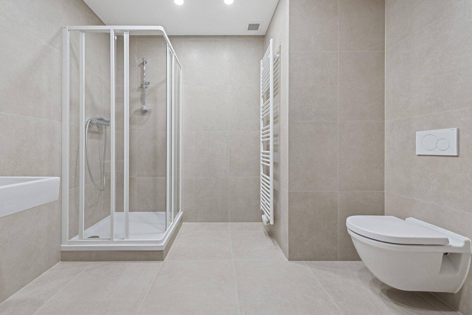 Modernes Badezimmer mit hellgrauen Fliesen, Duschkabine, wandhängendem WC und Handtuchheizkörper.