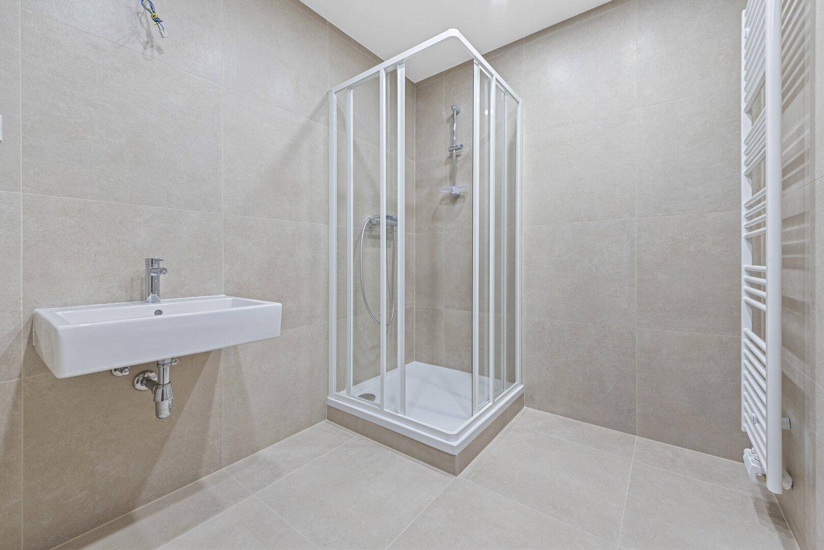 Modernes Badezimmer mit Duschkabine, Waschbecken, hellgrauen Fliesen und Handtuchheizkörper.