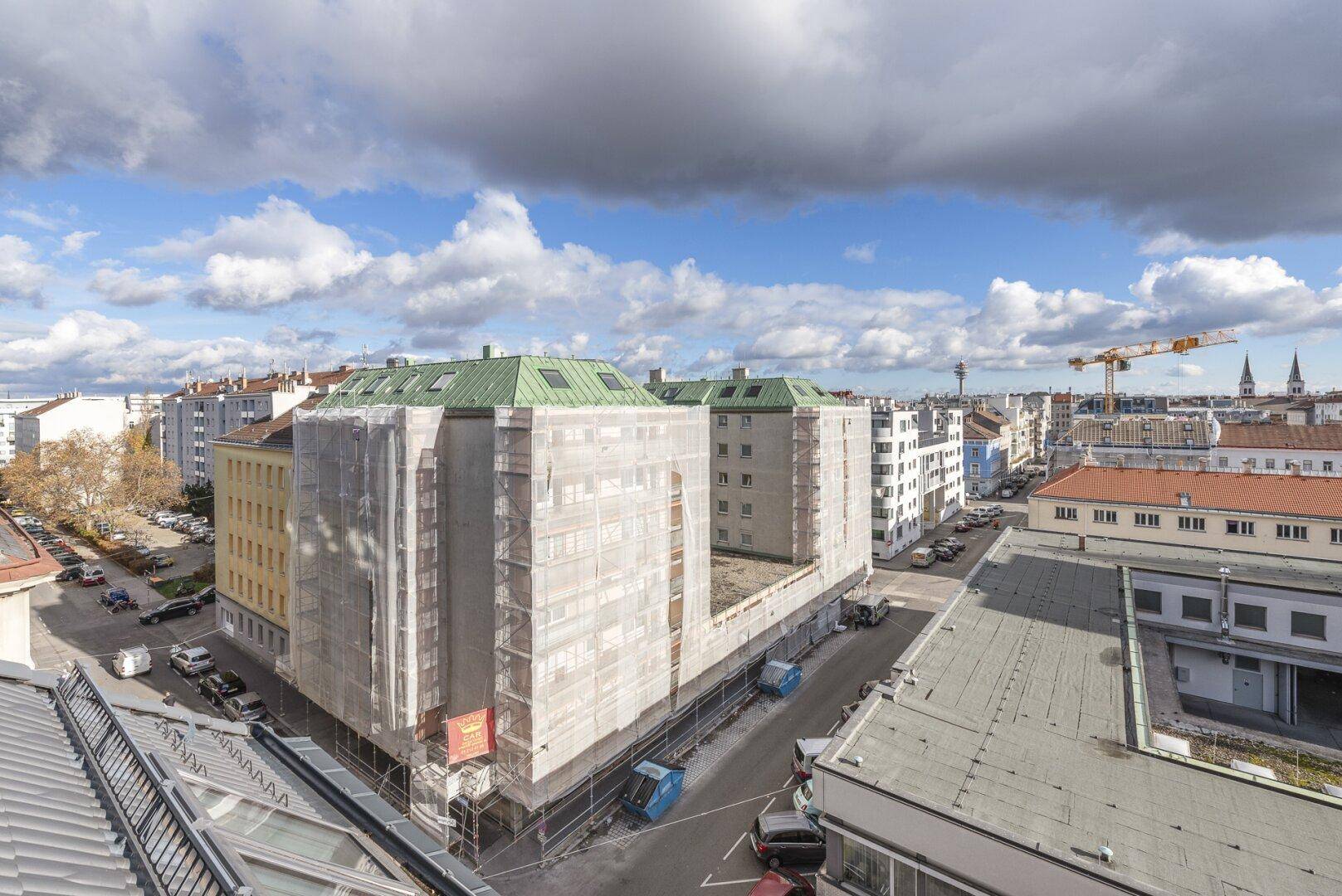 Weitläufiger Blick über die Dächer der Stadt mit Baustellen und Gebäuden unter bewölktem Himmel.