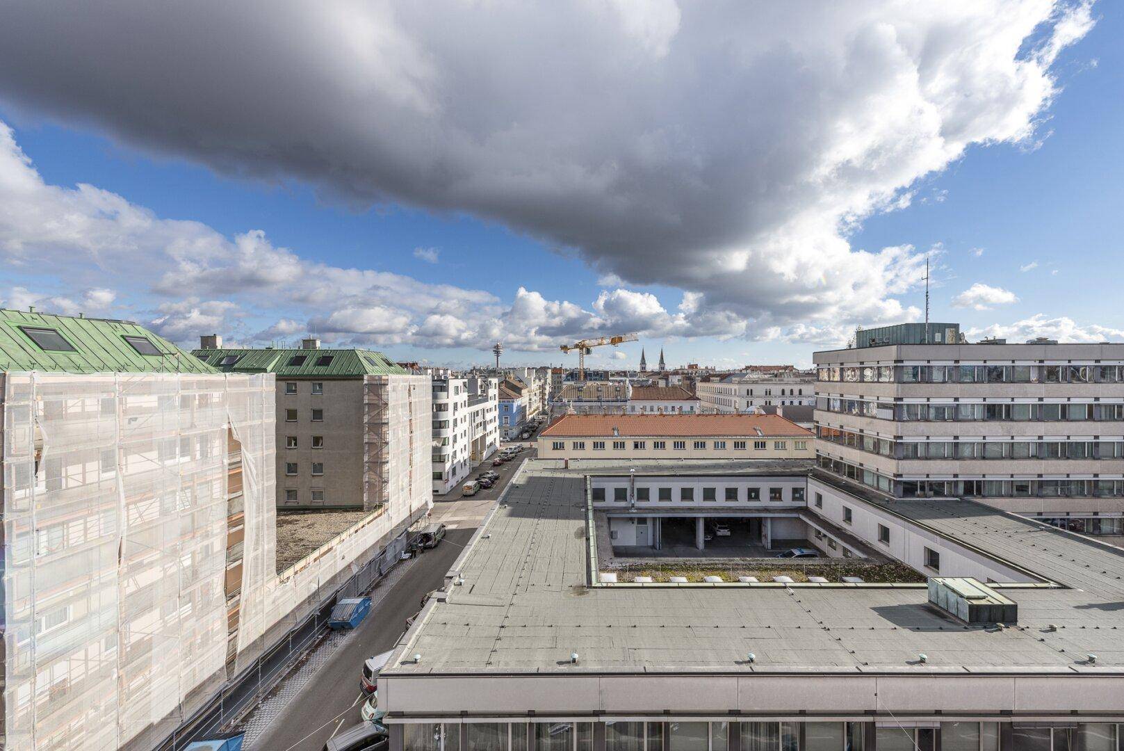 Panoramablick über die städtische Bebauung mit verschiedenen Dächern und Gebäuden unter bewölktem Himmel.