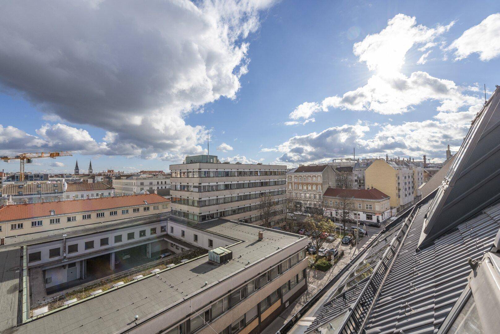 Sonniger Ausblick über die Dächer der Stadt mit blauem Himmel und Wolken.
