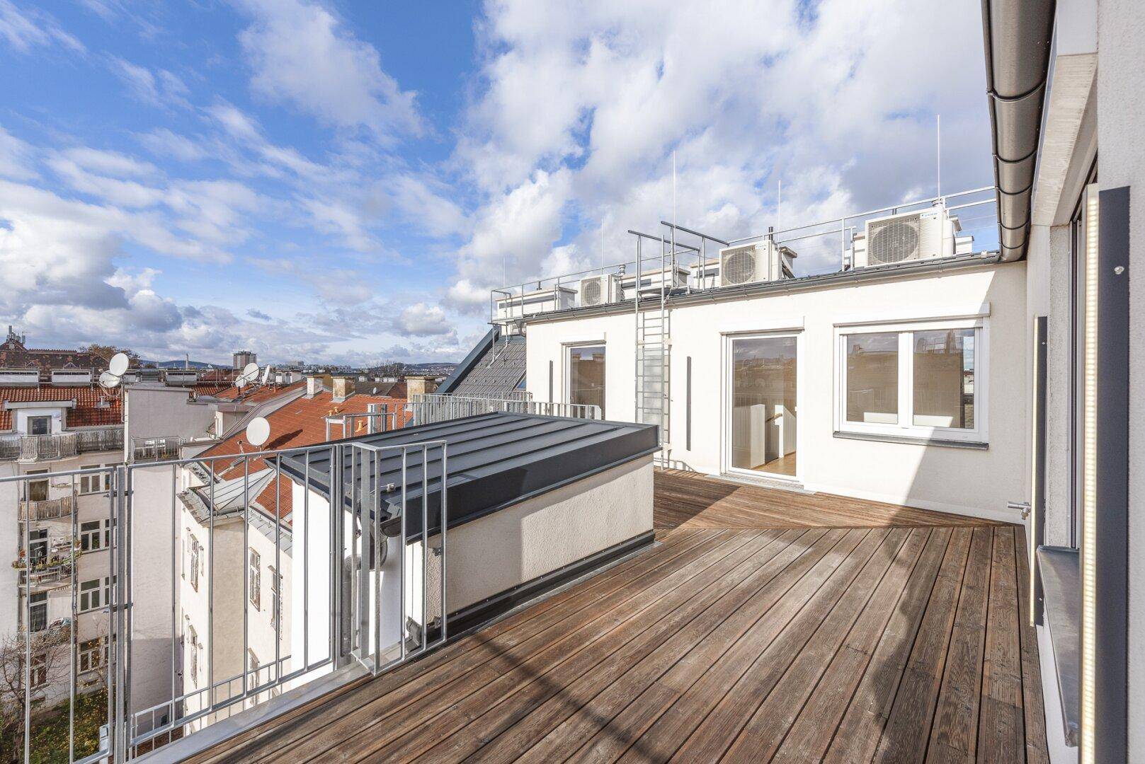 Geräumige Dachterrasse mit Holzboden, Metallgeländer und Blick über die Stadt.