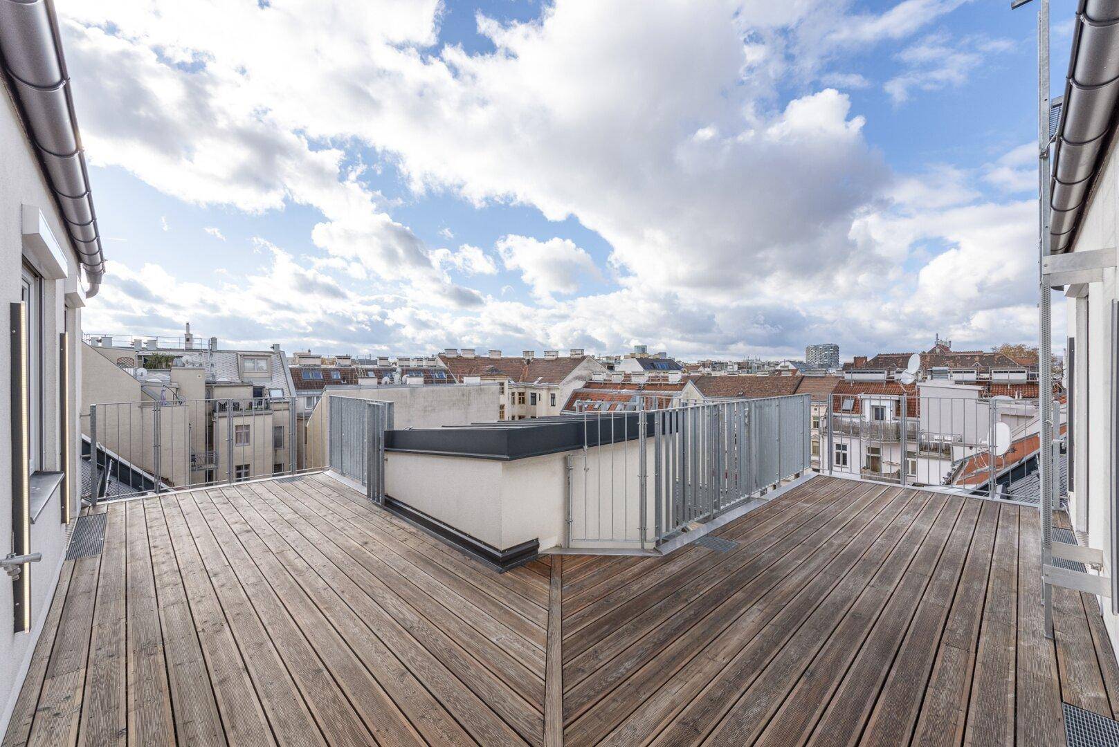 Weitläufige Dachterrasse mit Holzboden und modernem Metallgeländer unter blauem Himmel.
