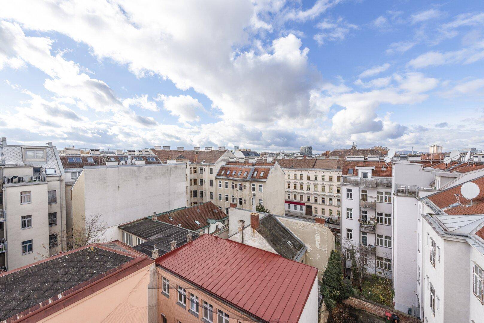 Blick über die Dächer der Stadt mit historischen Gebäuden und Wohnblocks unter bewölktem Himmel.