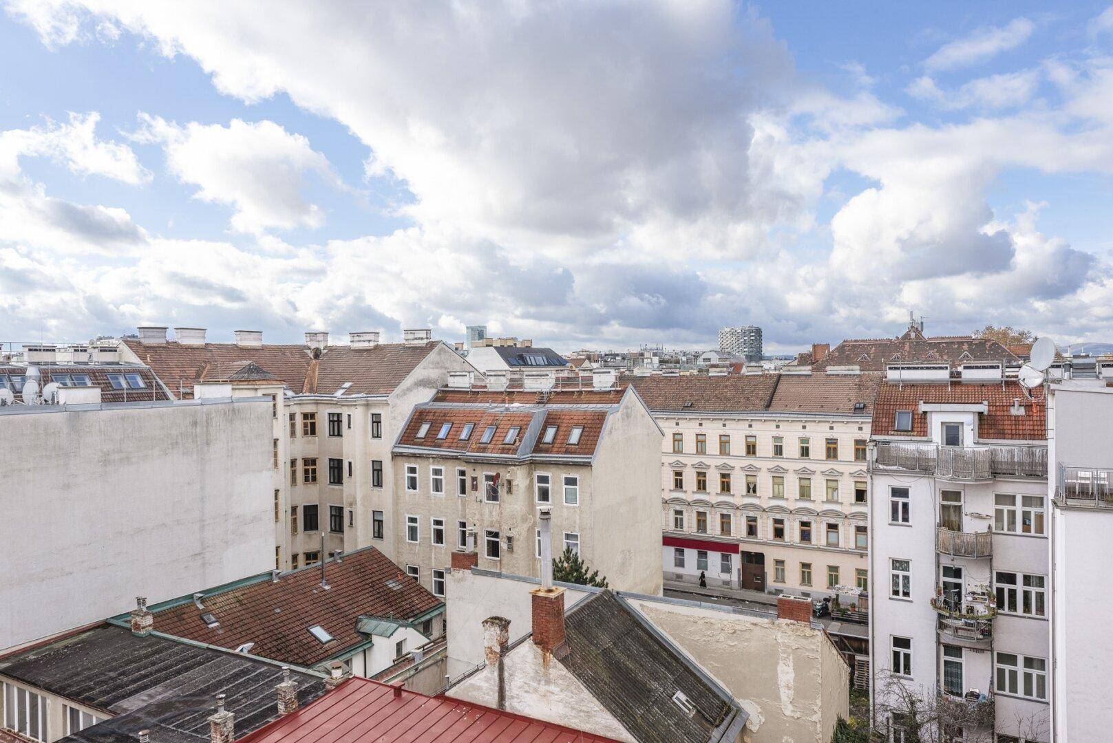 Weitläufiger Blick über die Dächer der Stadt mit verschiedenen Gebäudetypen unter bewölktem Himmel.