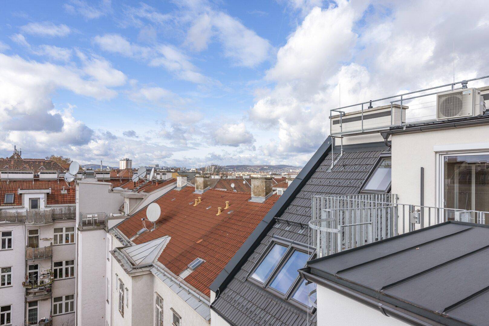 Panoramablick über die Dächer der Stadt mit einem modernen Dachgeschoss und traditionellen Ziegeldächern.