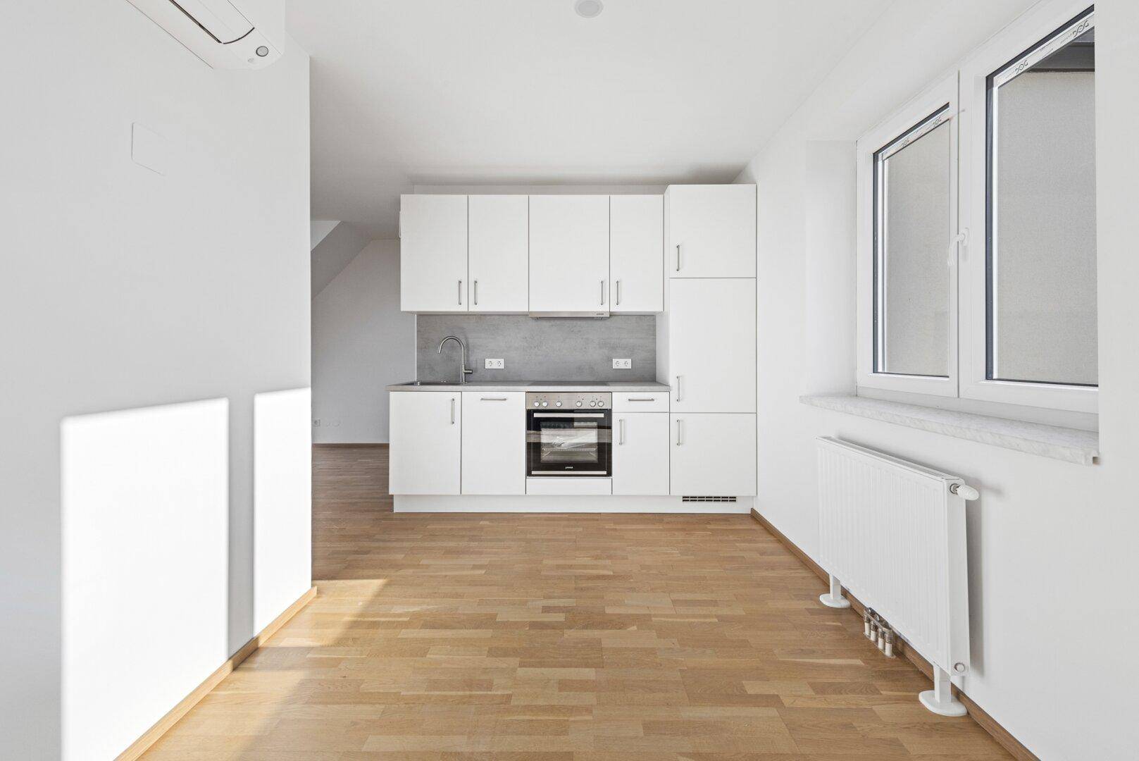 Moderne Einbauküche mit weißen Fronten, Holzboden und Klimaanlage in einem lichtdurchfluteten Raum.