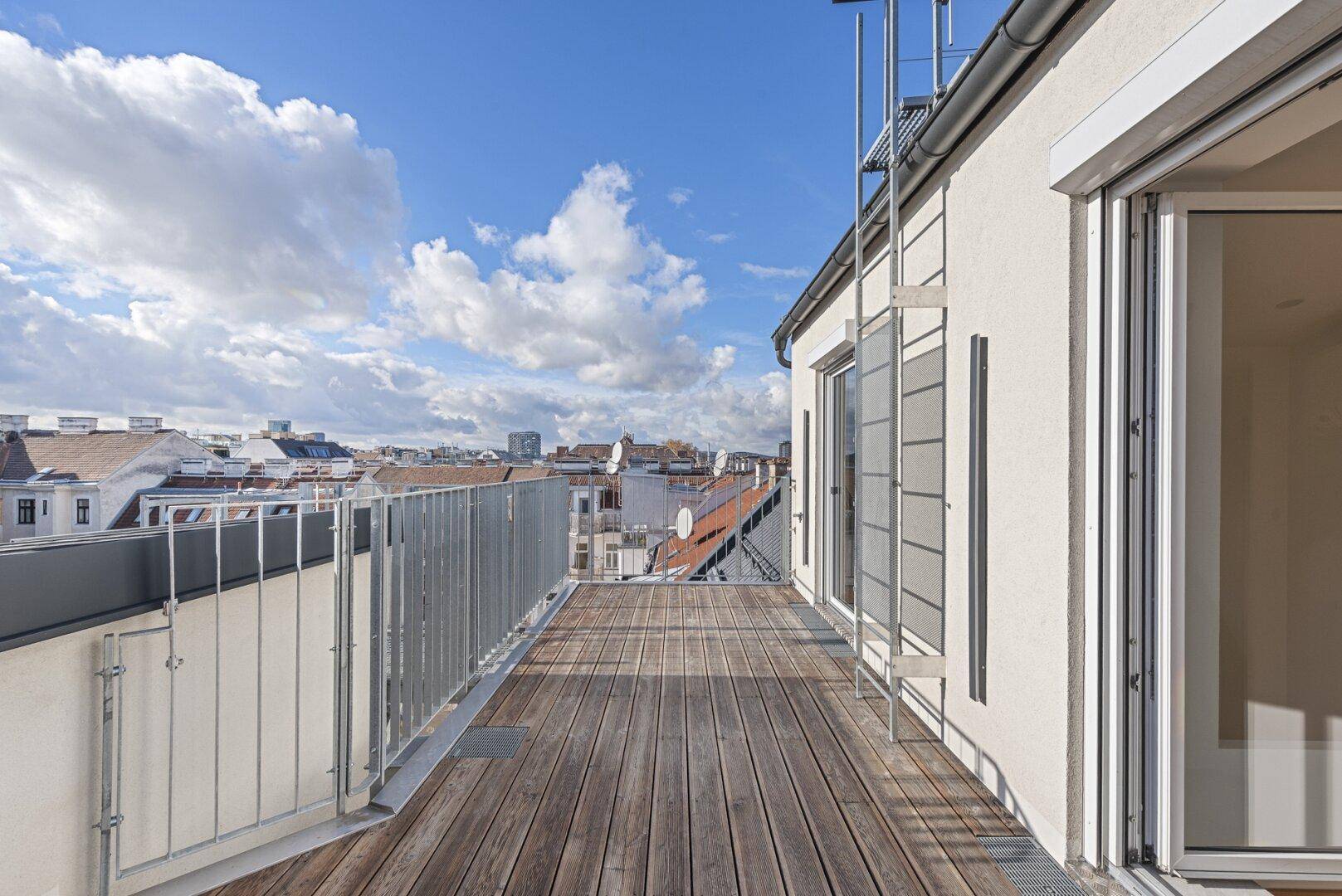 Sonnige Dachterrasse mit Holzboden, Metallgeländer und weitem Blick über die Dächer der Stadt.