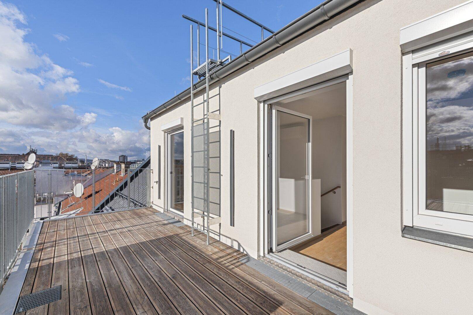 Geräumige Dachterrasse mit Holzdielen und Zugang zum Innenbereich, unter blauem Himmel.