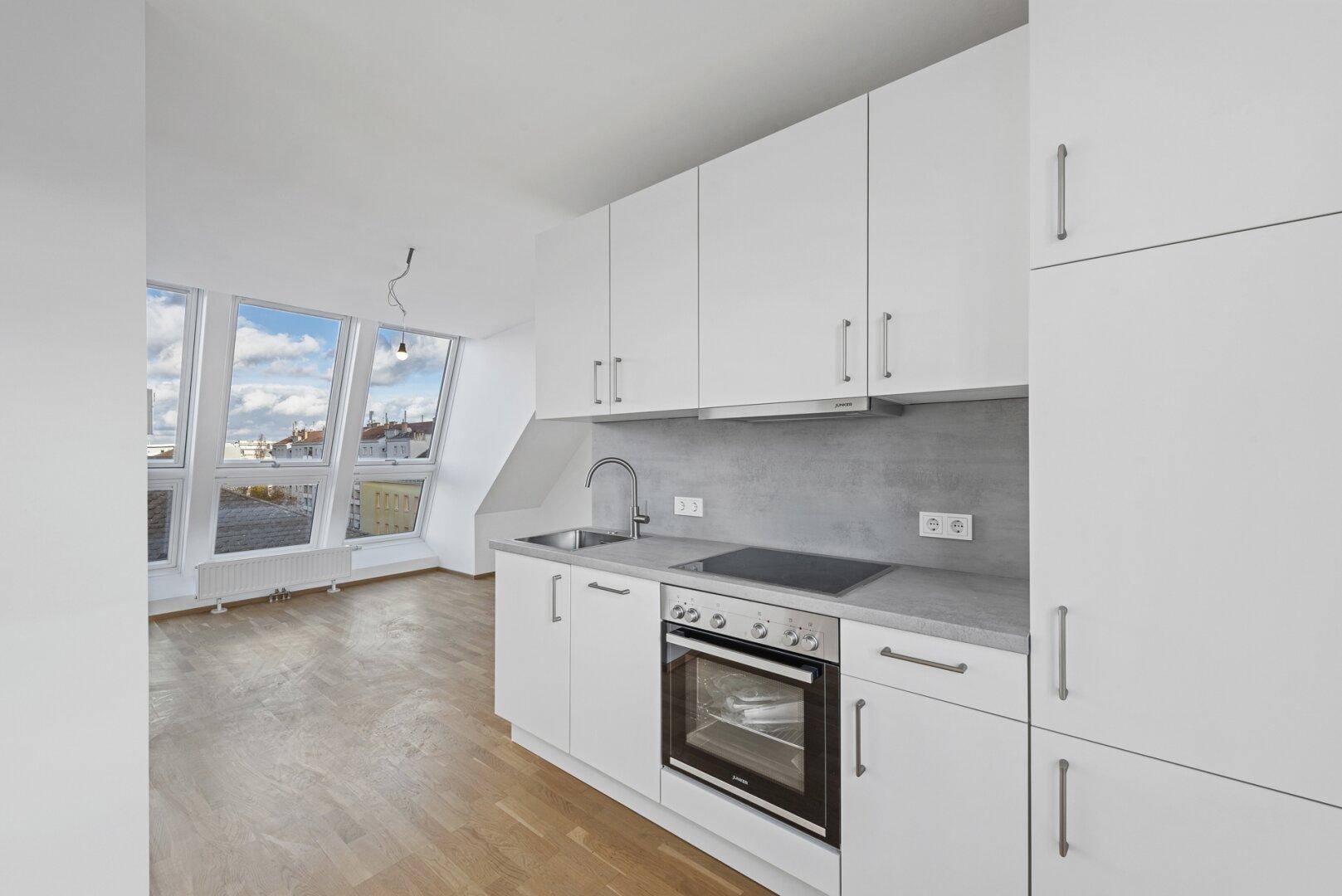 Moderne weiße Einbauküche mit Holzboden und Blick auf die Dächer der Stadt durch ein Fenster.
