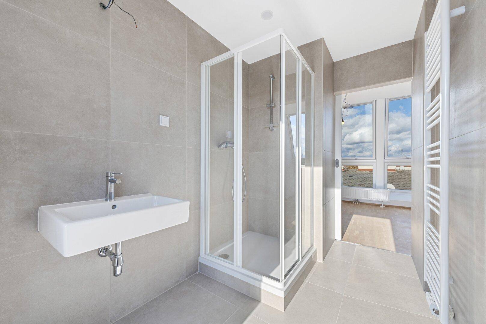 Modernes Badezimmer mit Duschkabine, Waschbecken und beheiztem Handtuchhalter in hellen Grautönen.