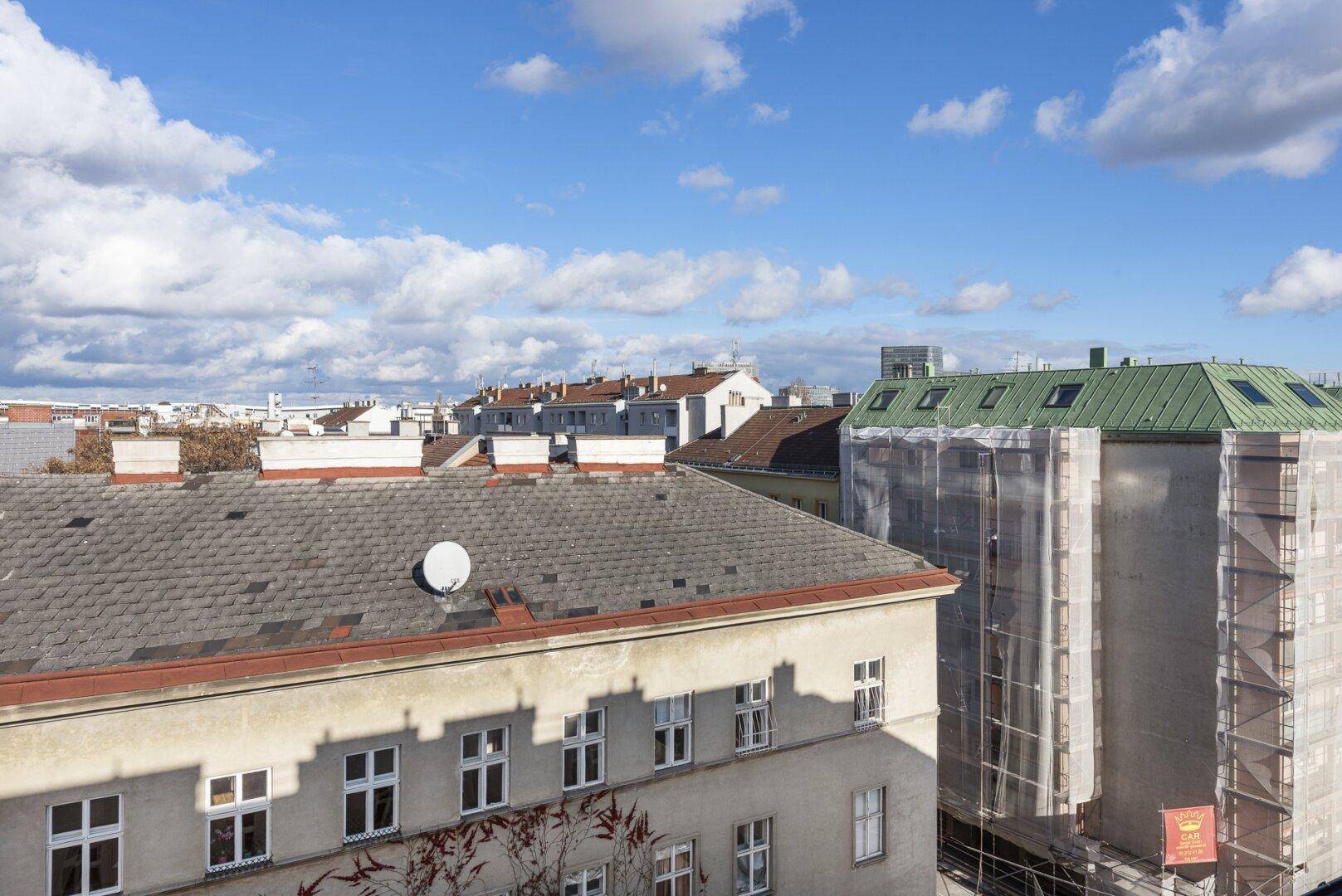 Blick über die städtische Dachlandschaft mit historischen Gebäuden und einem Neubau in der Ferne.