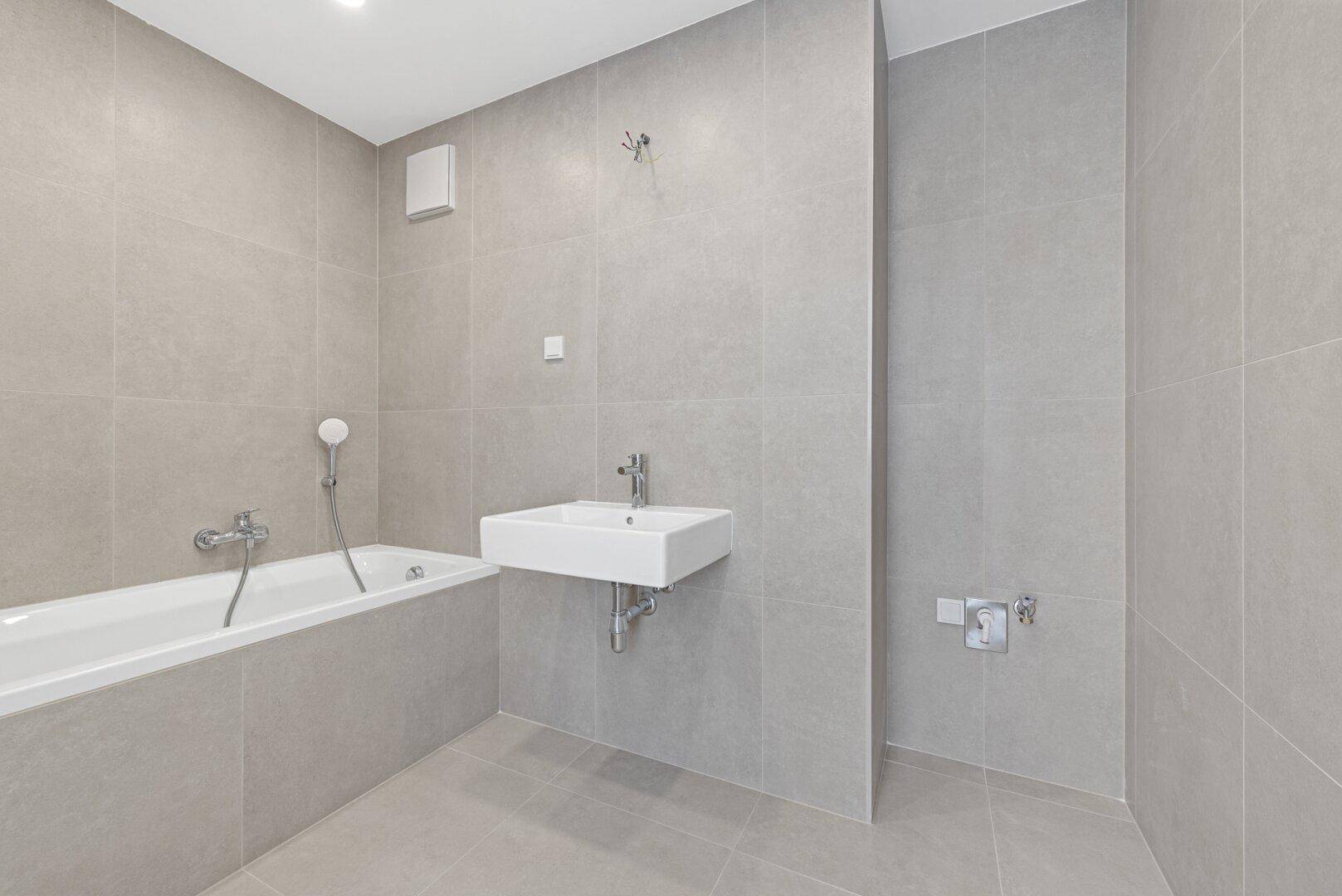 Modernes Badezimmer mit Badewanne, Waschbecken und großen hellgrauen Fliesen.