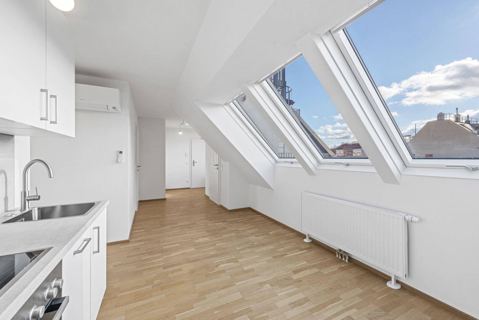 Helle Dachgeschosswohnung mit offener Küche, Parkettboden und großen Dachfenstern, die viel Licht hereinlassen.