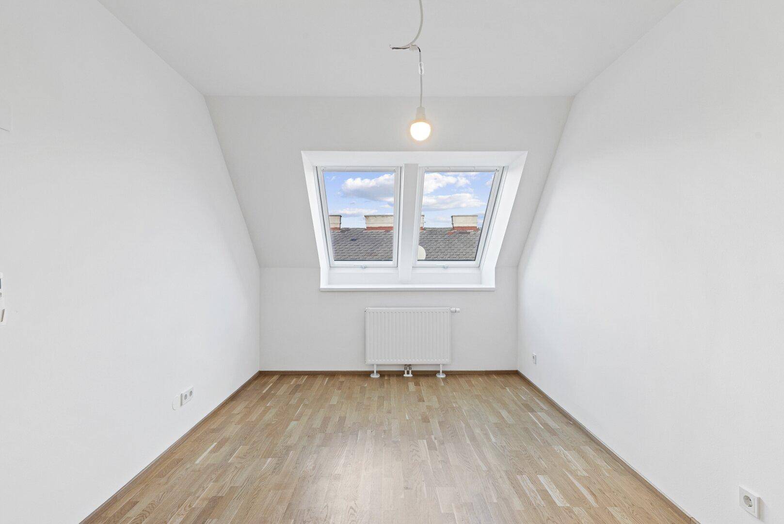 Lichtdurchflutetes Zimmer mit Parkettboden und zwei Dachfenstern, ideal als Schlaf- oder Arbeitszimmer.