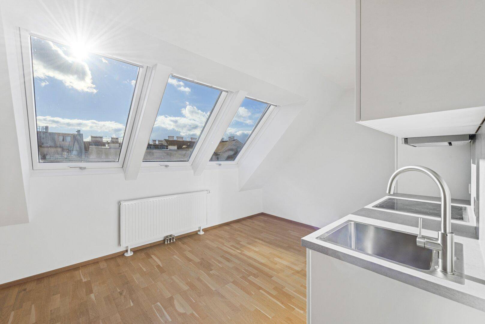 Heller Wohnbereich mit Parkettboden und großen Dachfenstern, die viel Sonnenlicht hereinlassen.