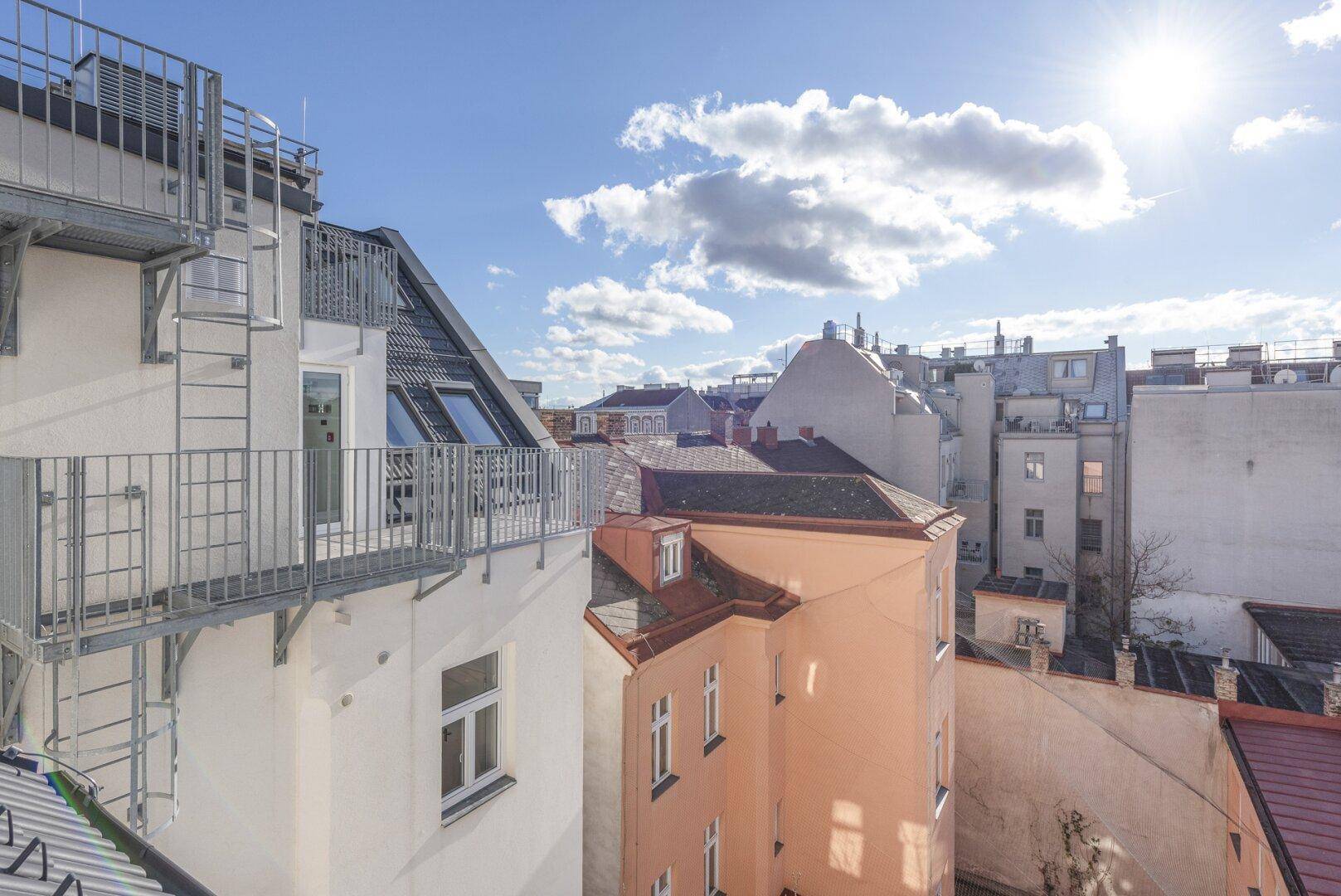 Dachterrasse oder Balkon mit Metallgeländer und Blick über die Dächer der Stadt.